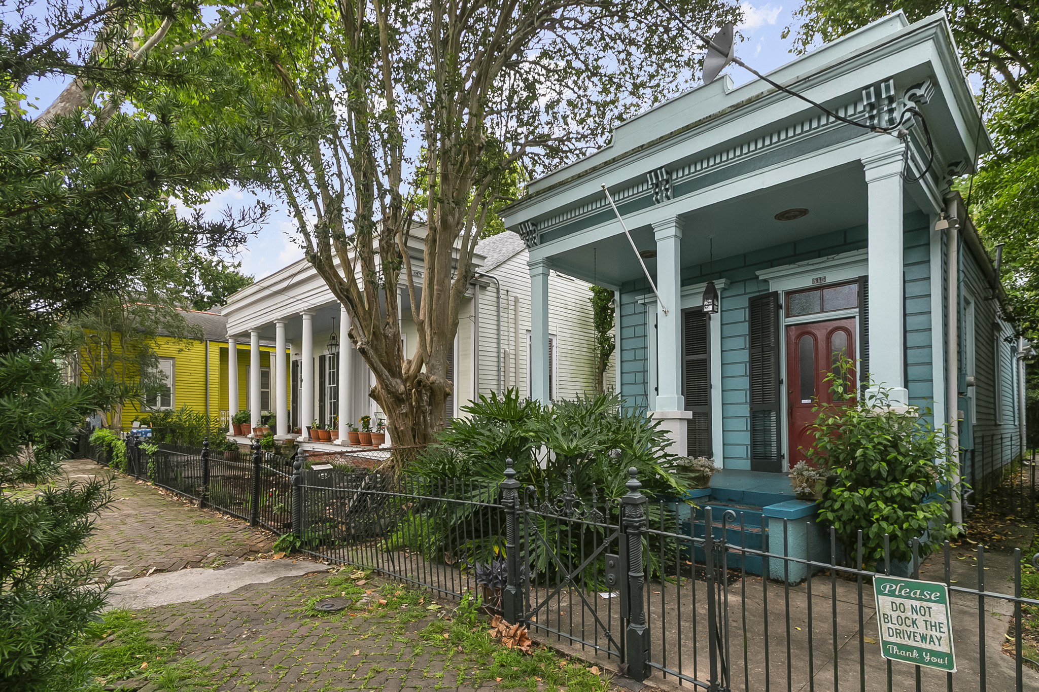 Row of colorful historic Uptown New Orleans homes with columned porches and cast-iron fences along a brick sidewalk